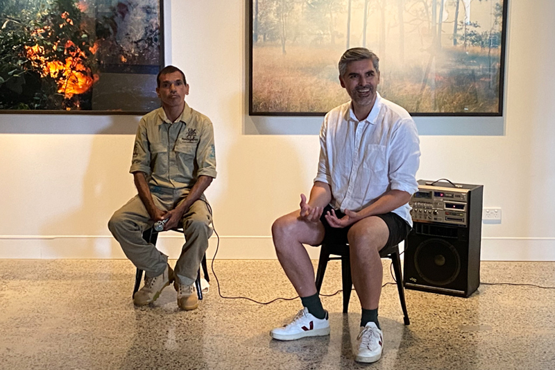 Matthew Stanton and Victor Bulmer sitting in the gallery with Matthew's artworks behind them