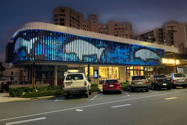Digital LED screen covering the facade at Bulmba-ja Arts Centre. The artwork is of 3 dugongs in white with black outlines and blue water.