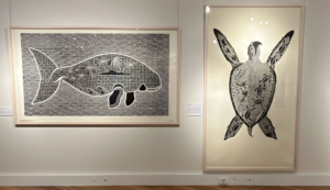 2 artworks handing on a white wall. They are framed in a light timber frame. The artworks are linocut prints on pages.