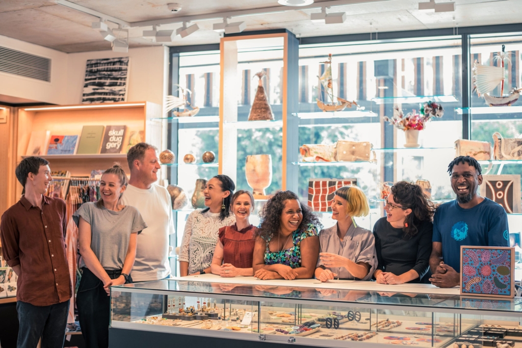 A group of 9 team member stand in a shop looking happy and smiling.
