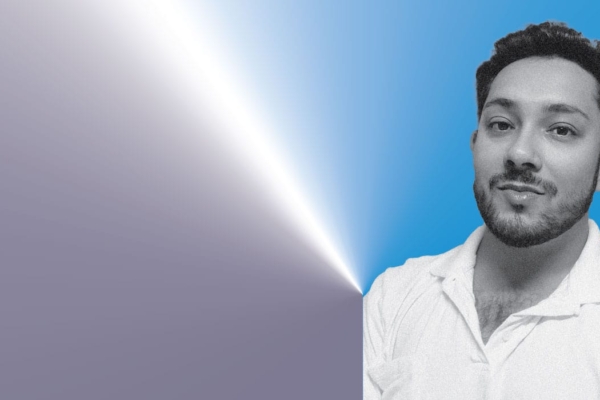 A black and white photo of a man standing wearing a white shirt. He looks directly at the camera.