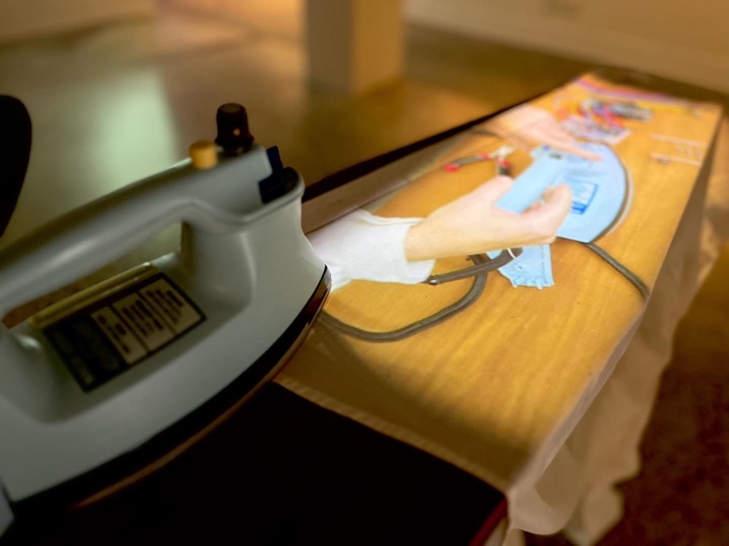 A retro iron sitting on an timber ironing board with a video projection directly onto the cloth that is placed on top of the ironing board.