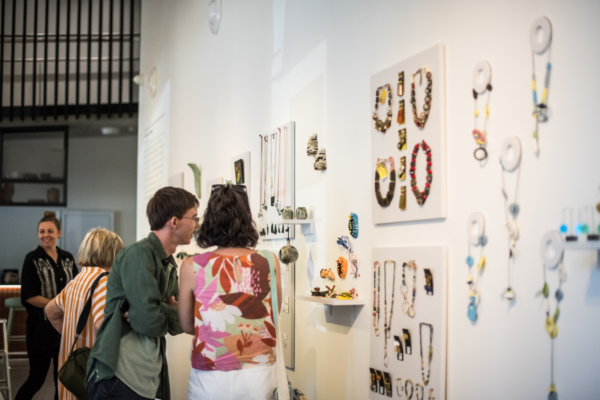 Several people looking at jewellery and objects on a gallery wall.