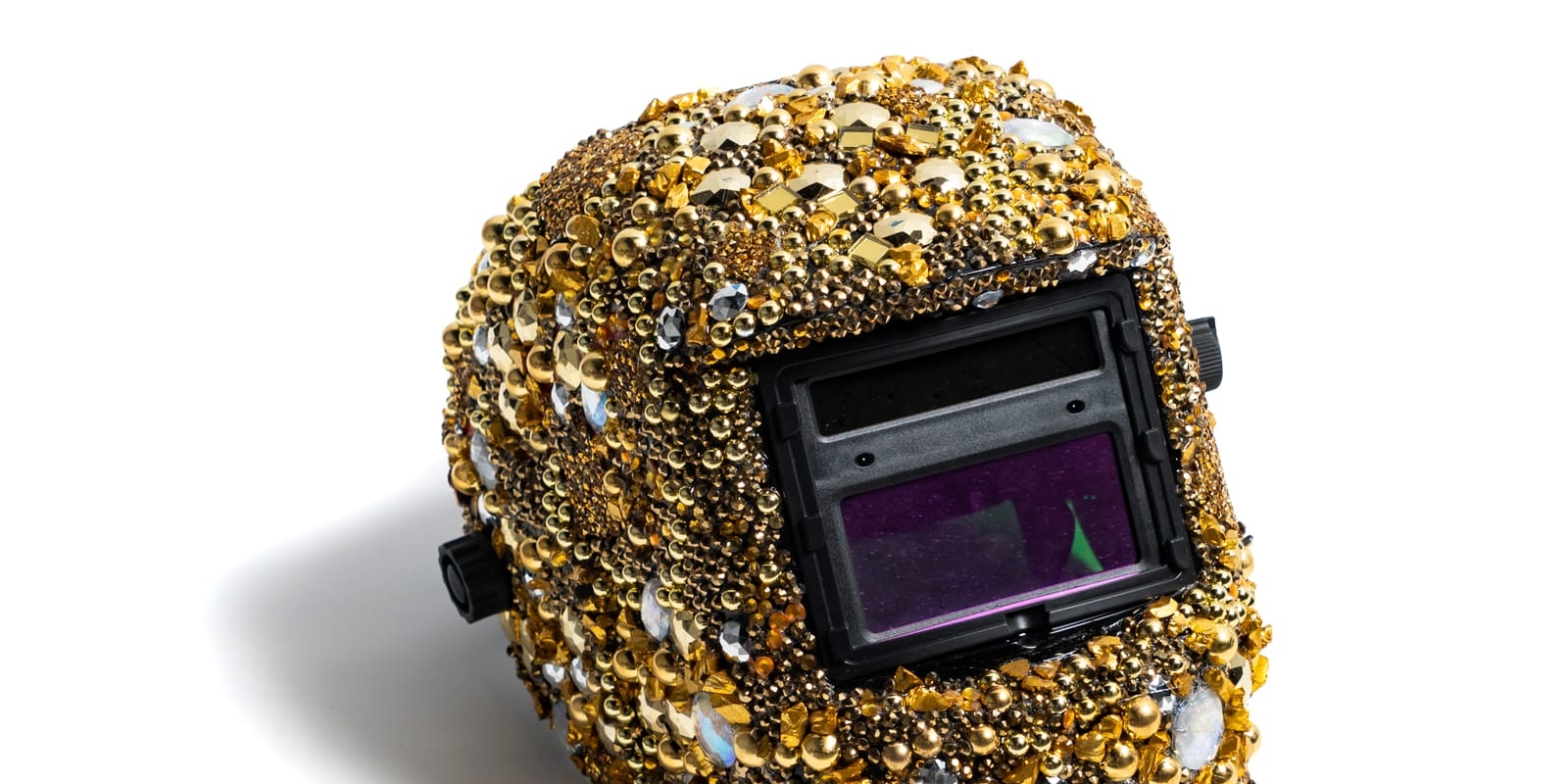 A welding helmet covered in gold jewels
