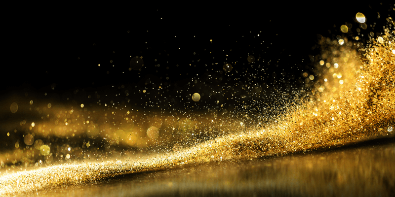 An image of gold glitter splashing on a glossy black surface.