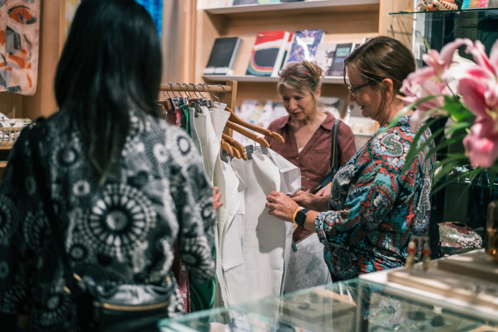 Three women looking at items in the NorthSite Store. Pink lilies are in the right corner.