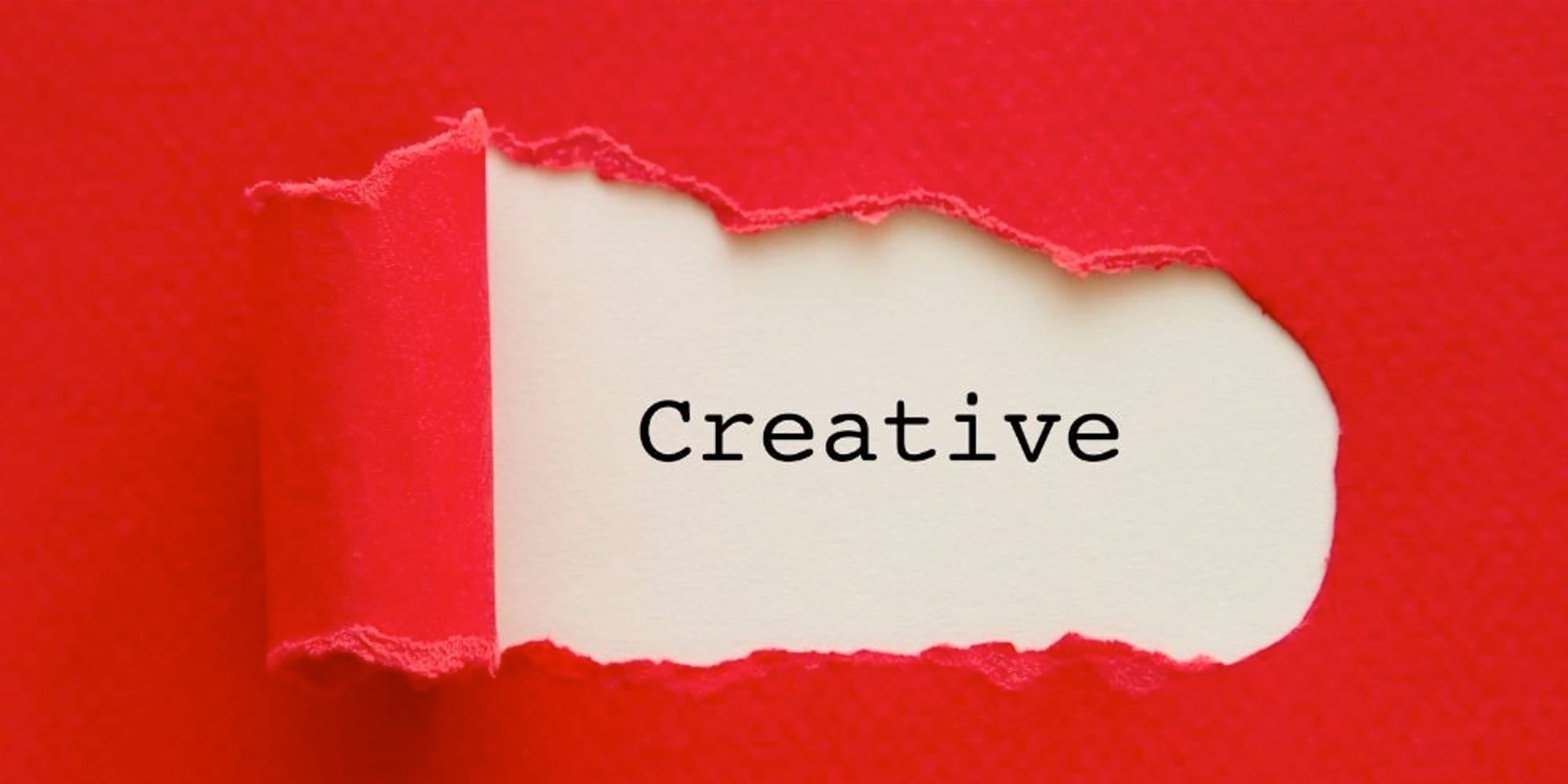 A red sheet of paper with a wrapped whole in the middle revealing the text 'creative' on white paper.