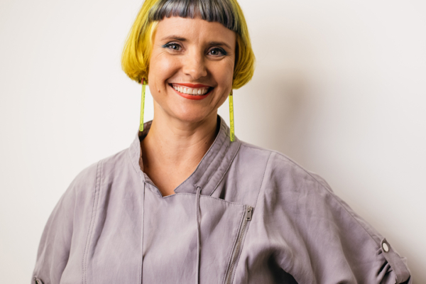 Melania stands looking at the camera with a smile.